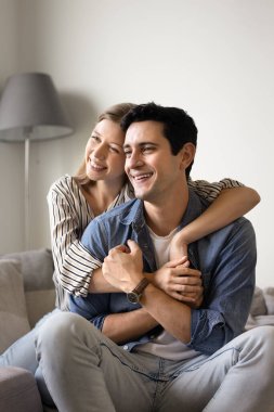 Mutlu genç Latin çift, sevgi, şefkat, şefkat, konforlu bir evde keyif çatıyor, yumuşak koltukta oturuyor, uzaklara bakıyor, gülümsüyor, gülüyor, dikey portre için poz veriyor.