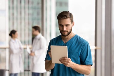 İşyerindeki modern dijital tableti kullanarak mavi üniformalı adam sağlık görevlisi, elektronik sağlık kayıtlarını inceliyor, hasta randevularını başvuru, mesajlaşma, koordinasyon personeli üzerinden ayarlıyor.