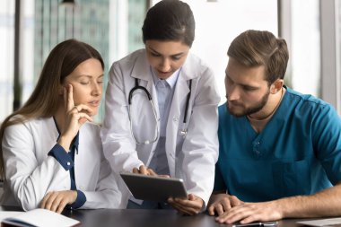 Hintli pratisyen hekimlerin liderliğindeki klinikte, tablet üzerindeki bilgileri inceleyen doktorlar, yeni uygulamaları açıklayarak, hasta verilerini göstererek, röntgen ve taramalar gibi tıbbi görüntüleri analiz ederek, tedavi planlarını tartışarak,