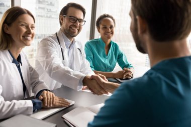 Çeşitli profesyoneller, sağlık çalışanları uzlaşmayı bitirir, konferans masasında el sıkışırlar, modern klinikte toplanırlar karşılıklı saygı gösterirler, anlaşma yaparlar, işbirliği ve güvenin işareti yaparlar.