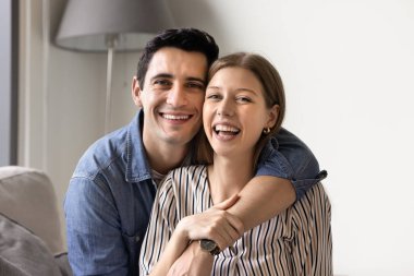 Neşeli, çekici, genç bir çift evde sarılıyor, portre için poz veriyor, dişlek tebessümlerle kameraya bakıyor, gülüyor, romantik bir ilişkiden keyif alıyor, aile eğlencesi, flört ediyor.