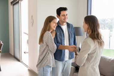 Mutlu, genç bir çift alıcı ya da kiracı emlakçıyla el sıkışıyor, yeni evin içinde duruyor, emlakçıya, emlakçıya, emlakçıya el sıkışıyor, gülümsüyor, anlaşmayı bitiriyor.