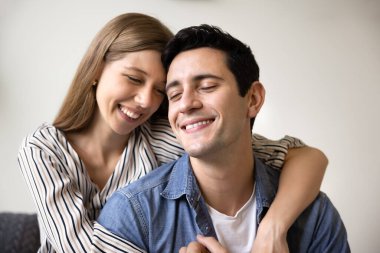 Şefkatle kucaklaşan, şefkatle gülümseyen, romantik ilişkiden zevk alan, evde boş boş vakit geçiren olumlu, genç bir çift. Mutlu eş kocayı kucaklıyor, arkadan dokunuyor.