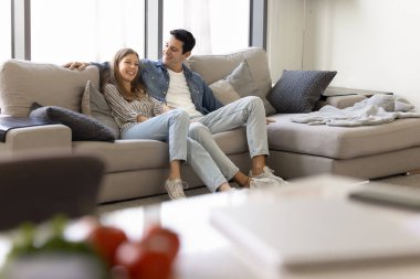 Genç ve mutlu bir Latin çift, rahat bir kanepede birlikte romantik vakit geçiriyorlar, sarılıyorlar, oturma odasındaki yumuşak geniş koltukta oturuyorlar, TV 'de film izliyorlar, sohbet ediyorlar, gülüyorlar.