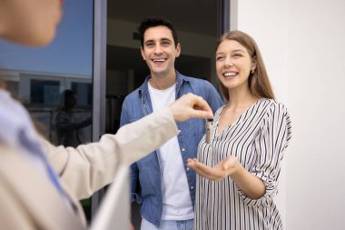Mutlu çift yeni ev alıyor, emlakçıdan anahtar alıyor, satıcıyla görüşüyor, apartman girişinde emlakçıyla görüşüyor. Pozitif genç adam ve kadın daire kiralamış.