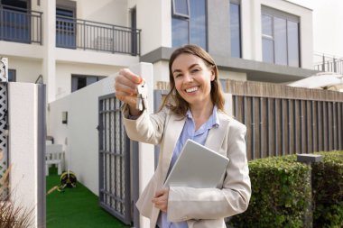 Yeni evden anahtar teklif eden mutlu emlakçı kadın ev, daire, kiralık ev kameraya bakıyor, gülümsüyor, iş portresi için poz veriyor.