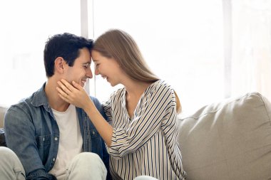 Neşeli, genç, tatlı İspanyol çift rahat bir evde romantik vakit geçiriyorlar, sarılıyorlar, kapalı gözlerle öpüşüyorlar, eğleniyorlar, gülüyorlar, kanepede oturuyorlar, gün ışığına karşı.