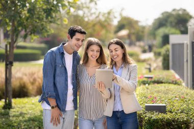 Birkaç müşteriye tablet üzerinde kira reklamları gösteren, kiracılara veya alıcılara banliyöleri gezdiren, müşterilerle çalışmak için modern teknolojiyi kullanan mutlu emlakçı.
