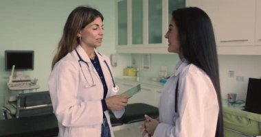 İki genç Latin doktor ultrason taramasını tartışıyor klinik ofisinde sonuç alıyorlar, danışmanlık yapıyorlar, birbirlerine mesleki destek veriyorlar, el sıkışıyorlar, gülümsüyorlar.