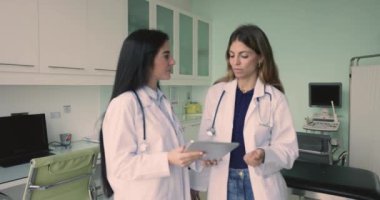 İki genç İspanyol kadın doktor ultrason tarama ofisinde konuşuyorlar, dijital tablet kullanıyorlar, ultrason taraması medikal araştırma, tıbbi teknoloji, kontrol elektronik sonuçları tartışıyorlar.