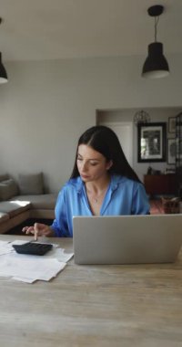 Makbuzları gözden geçiren, faturaları e-banka sistemiyle ödeyen, aylık bütçeyi sayan, harcamaları takip eden, oturma odasındaki masada oturan ev işleri yapan genç bir kadın. Mali yönetim