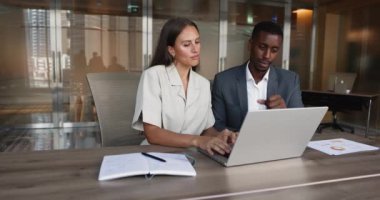 İki iş arkadaşı, Afrikalı işadamı ve Kafkasyalı kadın dizüstü bilgisayar kullanarak birlikte çalışıyor, yeni iş platformunu inceliyor, mali rapor verilerini analiz ediyor, gelecek toplantı için sunum üzerinde işbirliği yapıyorlar.