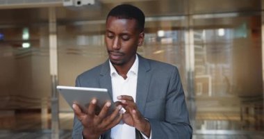 Resmi gri ceket giymiş, modern dijital tablet kullanan, yeni araçlar öğrenen, kurumsal yazılımları araştıran, proje yönetim platformunda ilerlemeyi izleyen Afrikalı iş adamının resmi.