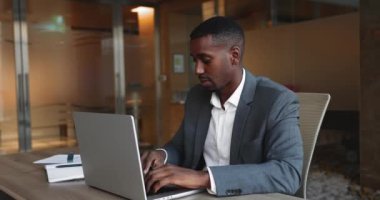 Afrikalı işadamı iş yerindeki dizüstü bilgisayarında işini başarıyla tamamlar, online görevi tamamlar, cihazı kapatır, sandalyeye yaslanır, üretken iş gününden sonra memnuniyet duygusu yayar.