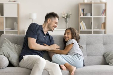 Mutlu küçük kız babasıyla kanepeye oturur, birlikte güler, oynar, birbirlerini gıdıklarlar, kaygısızca eğlenir, koşulsuz sevgiyi hisseder, okşar, evde şefkatli, neşeli anların tadını çıkarır.