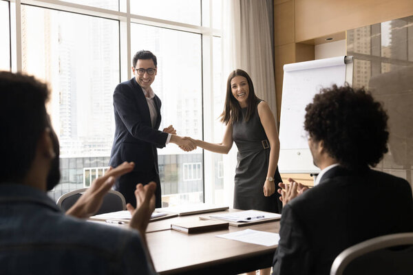 Arabian and European businesspeople shake hands at group meeting. Male boss congratulate employee with promotion, welcomes newcomer, praising, express respect for great work done. Business achievement