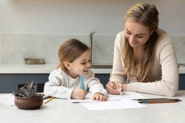 Mutlu anne, sevimli küçük kızına renkli kalemlerle albüm çizmeyi öğretiyor. Anne ve neşeli kız yaratıcı öğrenme oyunları oynuyor, sanat okuyor, kağıt albümlerde renkli karalamalar yapıyor.
