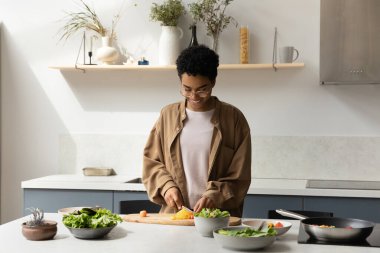 Mutlu Afro-Amerikalı aşçı kız sağlıklı yemek pişiriyor, evde taze sebze doğruyor, vejetaryen, vegan, çiğ yemek diyeti hazırlıyor, masada doğal malzemelerle gülümsüyor.