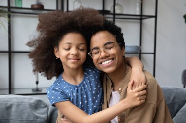 Minnettar bir Afrikalı anne, mutlu bir ergen kızı kucaklıyor, gözleri kapalı, neşe, şefkat, bağlılık, sevgi, annelik, boş zaman, sıcak bir aile ilişkisi hissediyor.