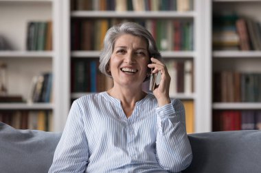 Neşeli, son sınıf öğrencisi bir kadın telefonla konuşuyor, cep telefonuyla konuşuyor, gülüyor, kanepede oturuyor, komik sohbetler yapıyor, iletişim kuruyor, iyi haberler alıyor.