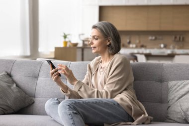 Dijital dünyayı keşfediyorum. Evde e-posta tipi cep telefonunda sanal iletişim kuran mutlu olgun bir kadın sohbet kitabı hizmetlerindeki arkadaşına mesaj gönderiyor akıllı telefon uygulaması kullanarak ürünleri internetten satın al