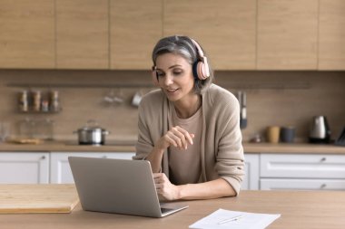 Mutfaktaki merkez ofis. Erken yaşta girişimci olan kadın girişimci dijital kulaklık takıyor sanal sohbette müşteriyle buluşuyor ve not defterindeki konferans uygulamasını kullanıyor.