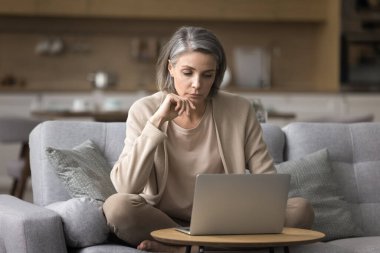 Serbest çalışmada sorun çözülüyor. Ciddi düşünceli, olgun iş kadını uzaktan çalışan ev ofisinin kanepesinde oturup araştırma projesini düşünen müşteri desteği e-postası oluşturan mesajları düşünen.