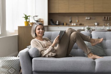 İyi kitapla rahatlıyorum. Portre mutlu, yaşlı, güzel, yetişkin bir kadın rahat koltukta uzanarak en sevdiği romanı okuyarak vakit geçiriyor. Yeni çok satan hikayenin tadını çıkarın. Kameraya gülümseyerek bakın. Boşluğu kopyala