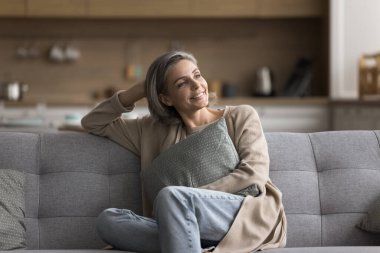 Evde mutlu. Kaygısız, olgun bir bayan rahat bir poz vermek için kanepeye oturur yastığa bakar dikkat çekme anının tadını çıkarır hafta sonu planlarında yalnız başına keyifli hayat değişiklikleri hayal edersin.