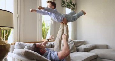 Babasının bacaklarına ve ayaklarına destek veren, yumruğu öne atılmış uçan süper kahramanı oynayan küçük bir çocuk. Mutlu baba ve oğul birlikte aktif oyunların keyfini çıkarıyorlar.