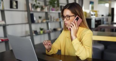 Güzel iş kadını dizüstü bilgisayar takıyor ve akıllı telefonla konuşuyor, müşteriyle sohbet ediyor, yardım veya bilgi sağlıyor modern çalışma alanındaki masada oturuyor, düzen kuruyor, uzaktan çalışıyor.