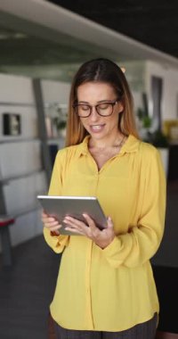 Güzel bir iş kadını elinde dijital tabletle çalışma alanında tek başına duruyor, çalışan iş başvurusunu kullanıyor, daktilo kullanıyor, işle ilgili konuları e-postalarla çözüyor, profesyonel dijital iletişimi yönetiyor.