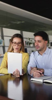 Dikey çekim, 30 'lu yaşlardaki iki genç meslektaşın dijital tablet üzerinde birlikte çalışırken çekildi. Kadın, erkek iş arkadaşına görev ya da kurumsal platformda yardım eder, verileri açıklar, gözden geçirir, takım çalışmasına katılır