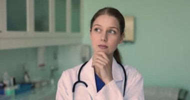 Düşünceli genç stajyer doktor kız beyaz önlük giyiyor, çenesine dokunuyor, başka tarafa bakıyor, tıp kariyerini düşünüyor, gelecekteki uzmanlığını düşünüyor, zor bir görev, sabırlı bir vaka, karar veriyor.