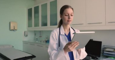 Klinikte dijital tablet kullanan odaklanmış genç doktor kadın, içeriği izliyor, gülümsüyor, gülüyor, hastayla internette sohbet ediyor, yüzünü çeviriyor, tıp alanında modern teknolojiyi düşünüyor.