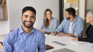 Genç 20 'li yaşlarda, arka planda meslektaşlarıyla birlikte masada oturan Arap erkek çalışanlar, yeterlilik, profesyonellik ve güvenilirlik yayıyor. Banka danışmanı, finansal danışman portresi. Kariyer