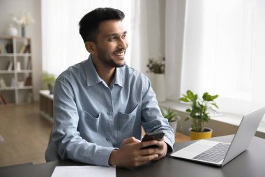 Ofiste cep telefonuyla iletişim kuran gülümseyen genç adam proje belgeleri üzerinde çalışmak için not defteri kullan. Mesaj metnini gözden geçir ve müşteriye mutlu bir şekilde geri bildirim oku.