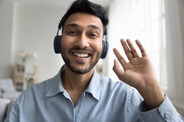 Merhabalar. Karizmatik gülümseme milenyum erkek profesyonel vlogger etkileyicisi modern kulaklıklar kayıt içeriği ev stüdyosundan video içeriği web kamera el dalga bakın merhaba seyirci aboneleri