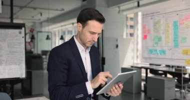 Ciddi İspanyol iş adamı web servisini kullanıyor, ofiste tek başına tablet yazıyor, sosyal medyada geziniyor, mutlu oluyor, neşeli oluyor, yüzünü çeviriyor, başarılı bir iş projesi üzerinde düşünüyor.