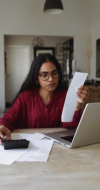 Hintli kadınların dikey görünümü kazanç ve giderleri hesaplar, elektronik banka sistemi kullanarak faturaları öder, aylık harcamaları takip eder dizüstü bilgisayarla ve yığınla finansal kağıtla masada oturur