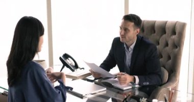 Erkek işveren, iş adamı, şirket yöneticisi patron masasında iş adayıyla konuşuyor, elinde kağıt özgeçmiş, özgeçmiş tutuyor, bayan Asyalı başvuru sahibine mesleki deneyimi soruyor.
