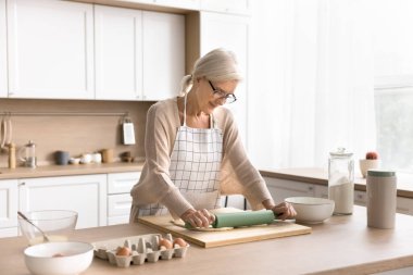 Mutlu ev hanımı. Sadece önlüklü orta yaşlı kadınlardan esinlenerek modern mutfakta mangır rulosu yapılır. Yaşlı eş sağlıklı yemek pişirmeyi, taze doğal ürünler kullanarak ekmek pizzası yapmayı sever.