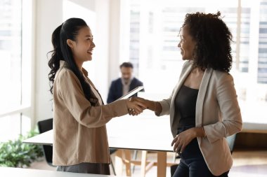 Pozitif, etnik çeşitlilikte genç iş ortağı kadınlar ofiste el sıkışıyor, toplantıyı bitiriyor, istişare ve tavsiyeler için teşekkür ediyor. İşe alım müdürü başarılı iş adayına el sıkışırken