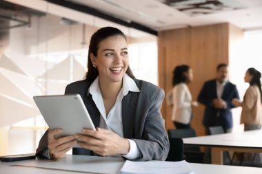 Ofiste ortak çalışma alanında tablet kullanan mutlu genç yönetici kadın, başka yere bakıyor, gülümsüyor, gülüyor, iş kariyeri başarısı üzerine düşünüyor, başarılı internet girişimi, modern teknoloji