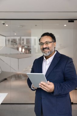 Ofiste elinde dijital tablet, yüzünü çevirmiş gülümseyen mutlu, olgun Hintli işadamı. İş öğretmeni, danışman, lider, uzman dikey portre