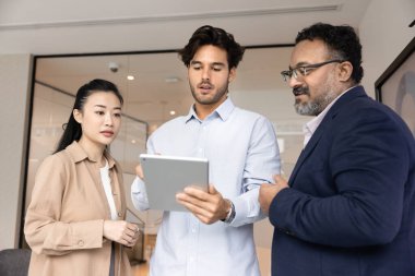 Kendine güvenen genç proje yöneticisi tablet üzerinde çeşitli meslektaşlara içerik gösteriyor, analizleri tartışıyor, çevrimiçi sunum yapıyor, tavsiye istiyor, iş web servisinin çalışmalarını anlatıyor