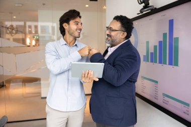 Mutlu farklı yaşlardaki iş arkadaşları yumruk tokuşturma hareketi yapıyor, tablet bilgisayar kullanıyor, başarılı online projeleri tartışıyor, internet pazarlama stratejisi, takım çalışması, konuşuyor, gülüyor.