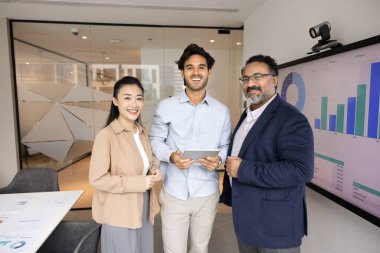 Mutlu çok ırklı farklı yaş grubu ofis sunum odasında birlikte poz veriyor. Büyük tahta, duvar ekranı, kameraya bakıyor, takım çalışması için buluşuyor, gülümsüyor.