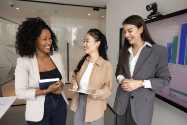 Ofis toplantı odasında konuşan ve gülen üç neşeli genç bayan meslektaştan oluşan çeşitli bir grup proje, pazarlama stratejisi, eğlenceli takım çalışması, eğlenceli çalışma molaları hakkında yaratıcı fikirleri tartışıyor.