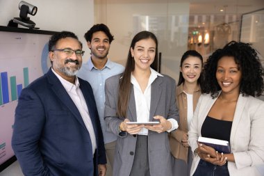 Çok ırklı, farklı etnik çeşitlilikte iş dünyası pazarlama ekibi ve ofis yönetim kurulunda portre için bekleyen genç bayan lider, kameraya bakıyor, gülümsüyor, gülüyor, birlikte poz veriyorlar.
